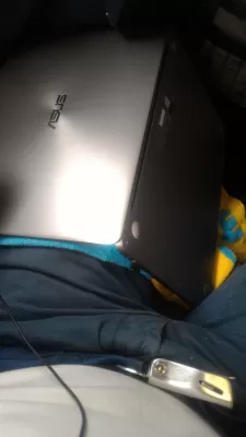 Deversare lichidă pe un laptop: Ce să faci? Ghid complet pentru recuperarea laptopului! : Ținând un laptop cu capul în jos pe picior în timpul unui zbor cu un prosop apăsat împotriva tastaturii pentru a mări lichidul Aperol spritz vărsat pe laptop